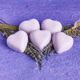 Five purple heart soaps on top of lavender springs, on a purple cloth. lavender says self care and hearts say self love. Self care and self love are essential for caretakers.
