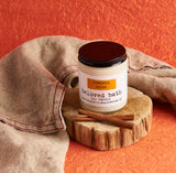 Pumpkin Spice Candle on a round piece of wood with cinnamon sticks surrounded by a burlap cloth with an orange background. 